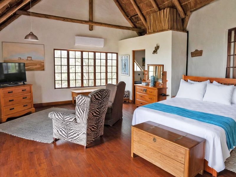 Spacious bedroom featuring a high vaulted thatched ceiling with exposed timber rafters, timber flooring, and large windows providing natural light.