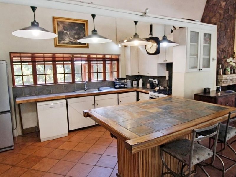 A functional kitchen featuring a large tiled island, ample built-in cabinetry, double sink, and warm terracotta floor tiles with natural light.