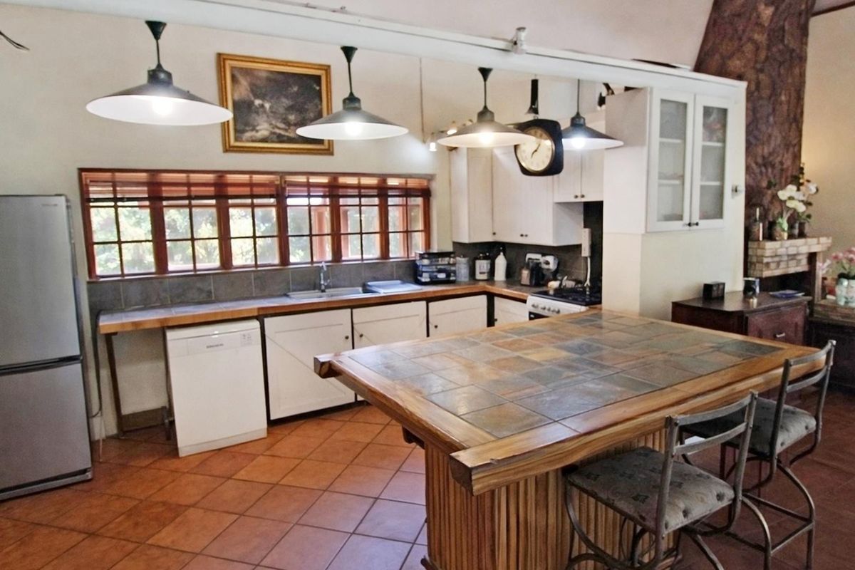 A functional kitchen featuring a large tiled island, ample built-in cabinetry, double sink, and warm terracotta floor tiles with natural light.