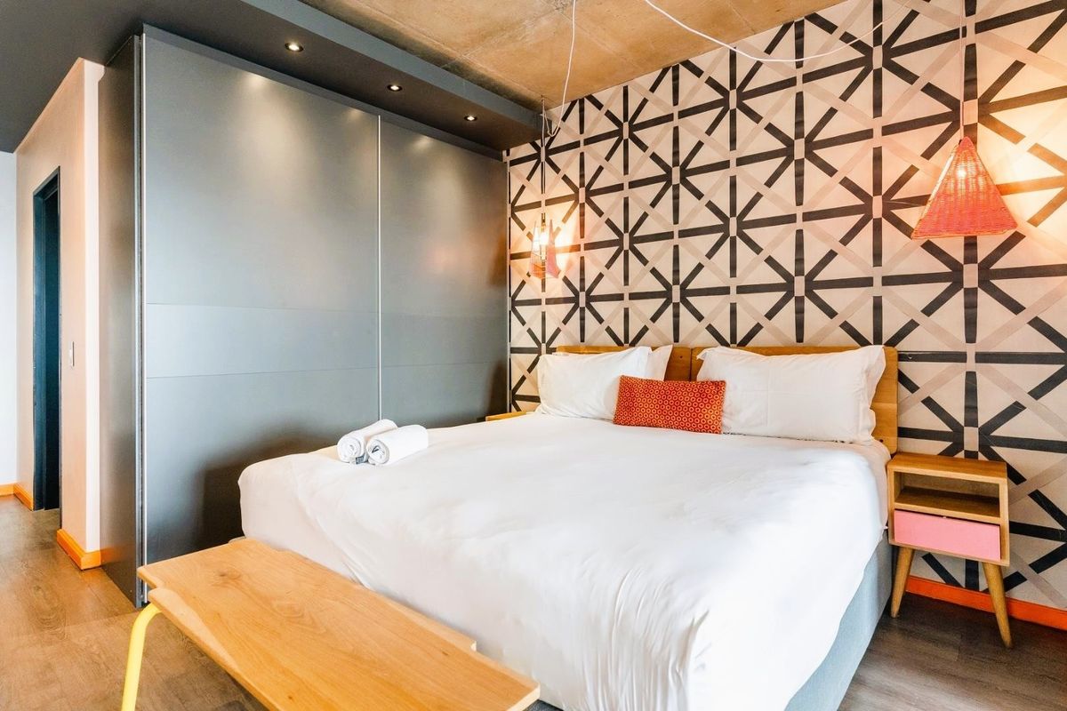 Modern bedroom featuring an exposed concrete ceiling, built-in wardrobe with integrated lighting, and decorative geometric wall paneling.