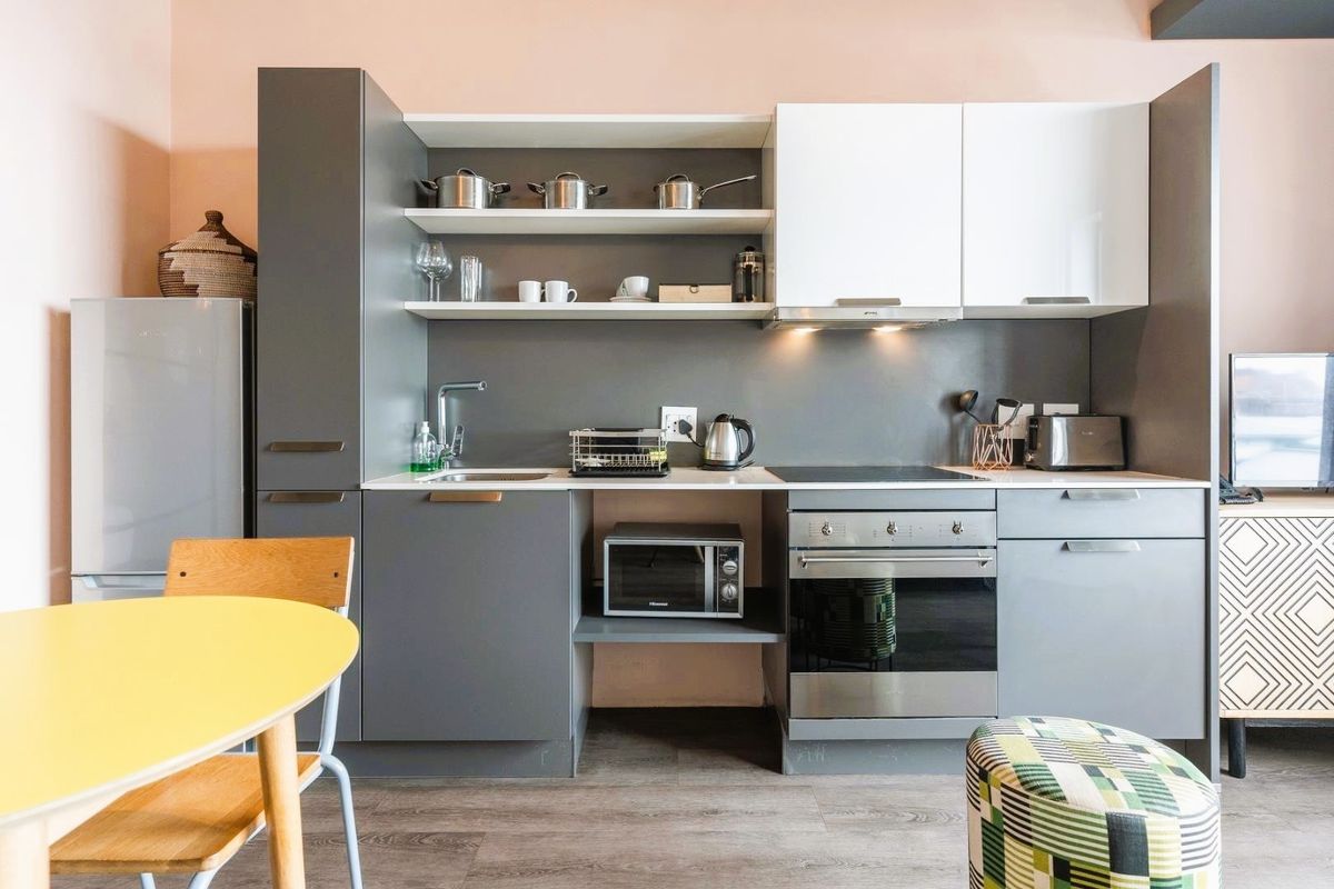 Modern compact kitchen featuring grey and white cabinetry, integrated oven, electric cooktop, extractor fan, and open shelving with a clean, contemporary finish.