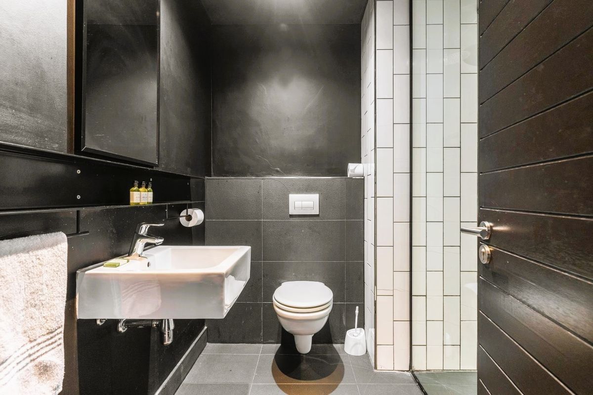 Modern bathroom featuring a wall-mounted basin, wall-mounted toilet, and contrasting dark and white tiled finishes.