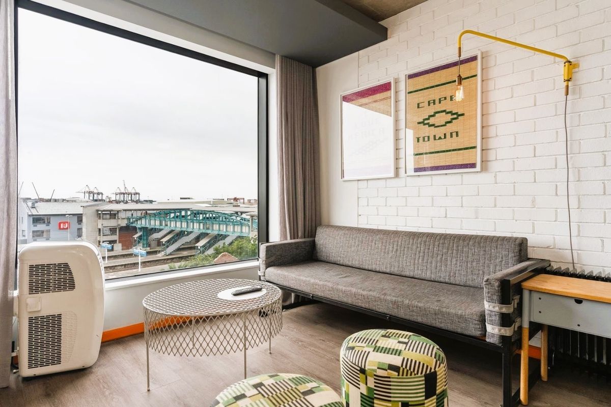 A modern living room featuring a large window with urban views, exposed brick wall, and contemporary finishes.