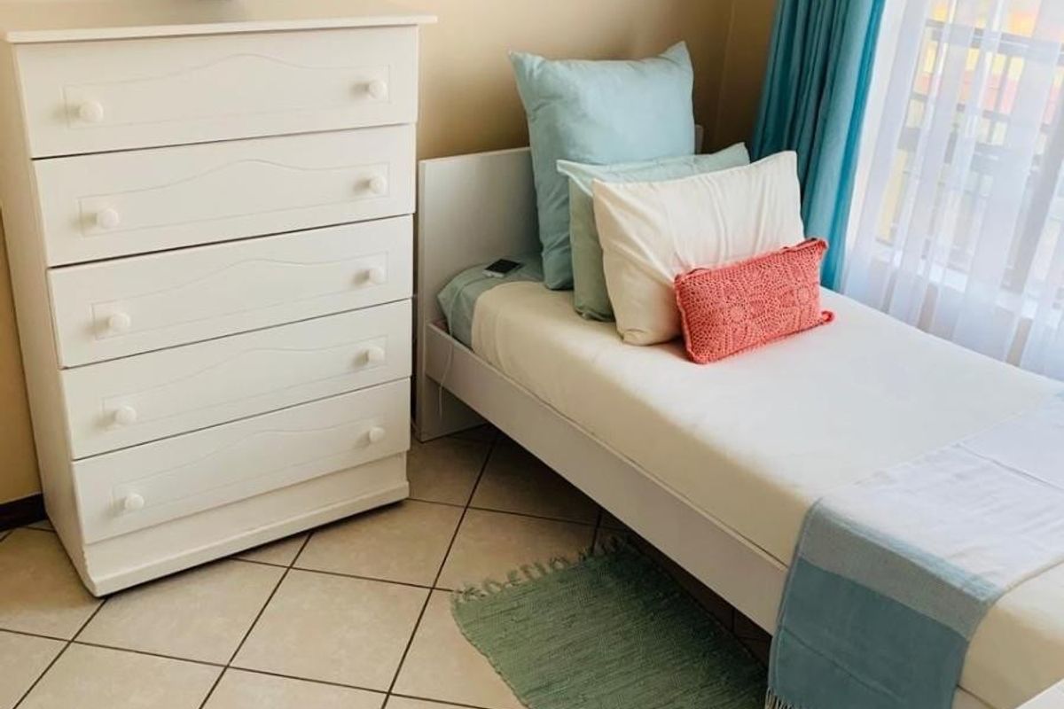 A compact bedroom featuring neutral tiled flooring and large windows with curtain treatments, providing a functional and well-lit living space.