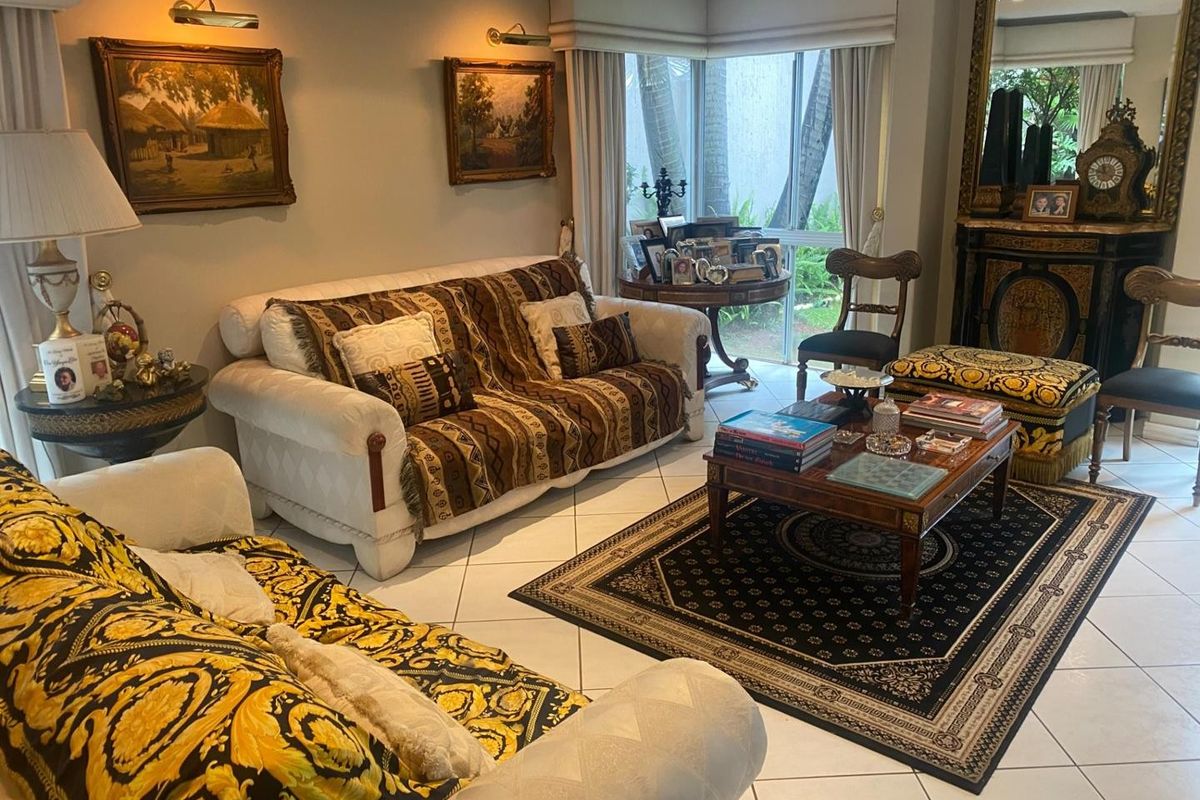 A traditional living room featuring tiled flooring, a built-in fireplace, and large windows providing natural light and garden views.
