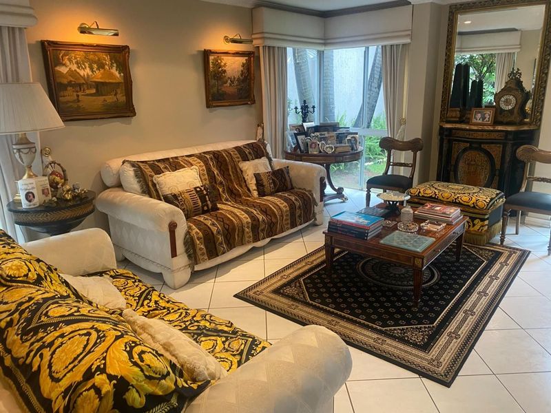 A traditional living room featuring tiled flooring, a built-in fireplace, and large windows providing natural light and garden views.
