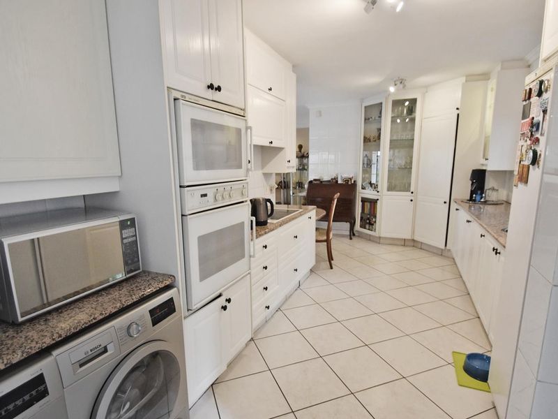 A functional kitchen featuring white cabinetry, granite countertops, built-in oven and microwave, and tiled flooring with ample storage space.