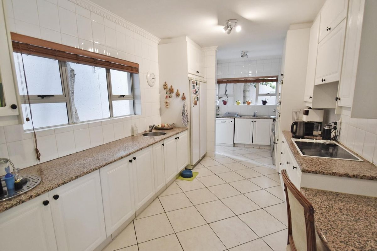 A functional kitchen featuring white cabinetry, granite countertops, tiled backsplash, and ceramic tile flooring, with a separate scullery area visible in the background.