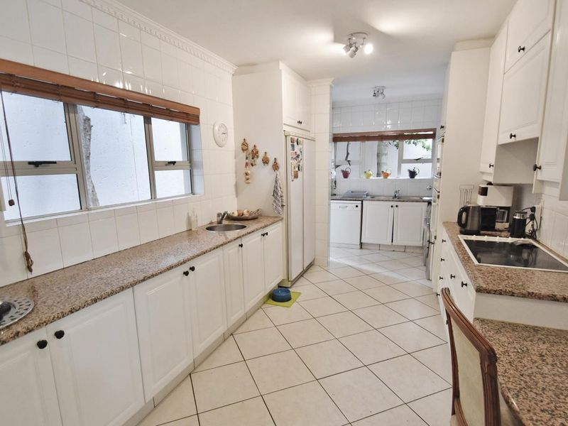 A functional kitchen featuring white cabinetry, granite countertops, tiled backsplash, and ceramic tile flooring, with a separate scullery area visible in the background.