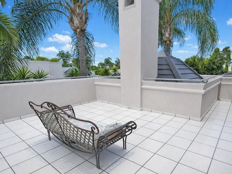 Spacious open-air balcony featuring white tiled flooring, a central masonry chimney stack, and metal safety railings with views of the surrounding area.