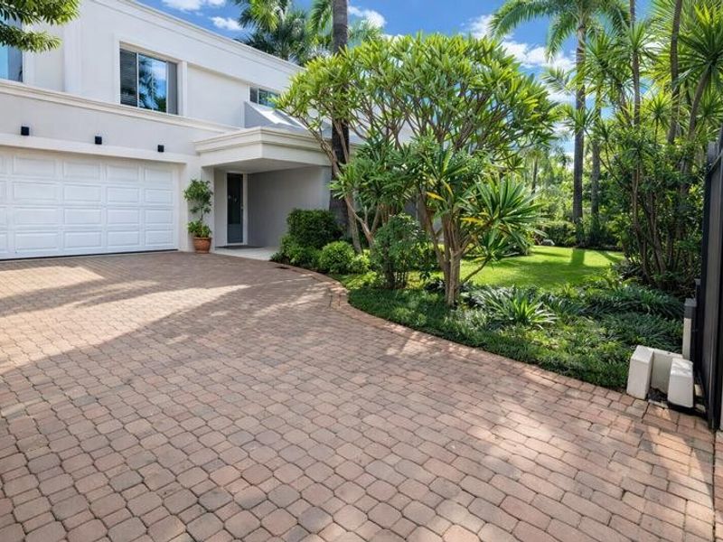 A well-maintained front exterior featuring a paved driveway, a modern sectional garage door, and lush landscaped gardens.