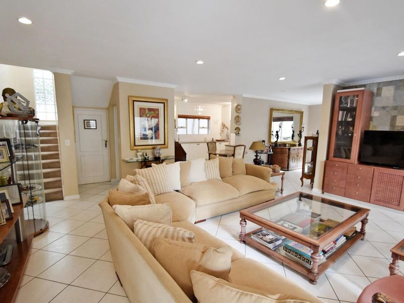 Spacious open-plan living area featuring tiled floors, recessed lighting, a stone feature wall, and an integrated staircase leading to the upper level.