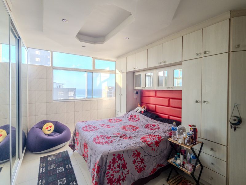 A bedroom featuring extensive built-in cabinetry, a recessed ceiling design, and large windows offering natural light and coastal views.