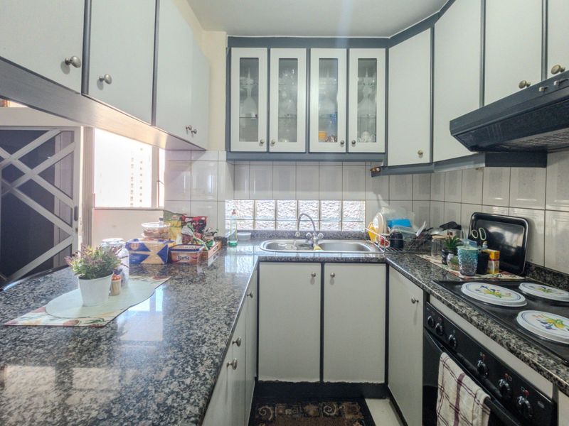 Compact kitchen featuring granite countertops, built-in cabinetry with glass-front uppers, a stainless steel sink, and a built-in cooktop with an extractor fan.