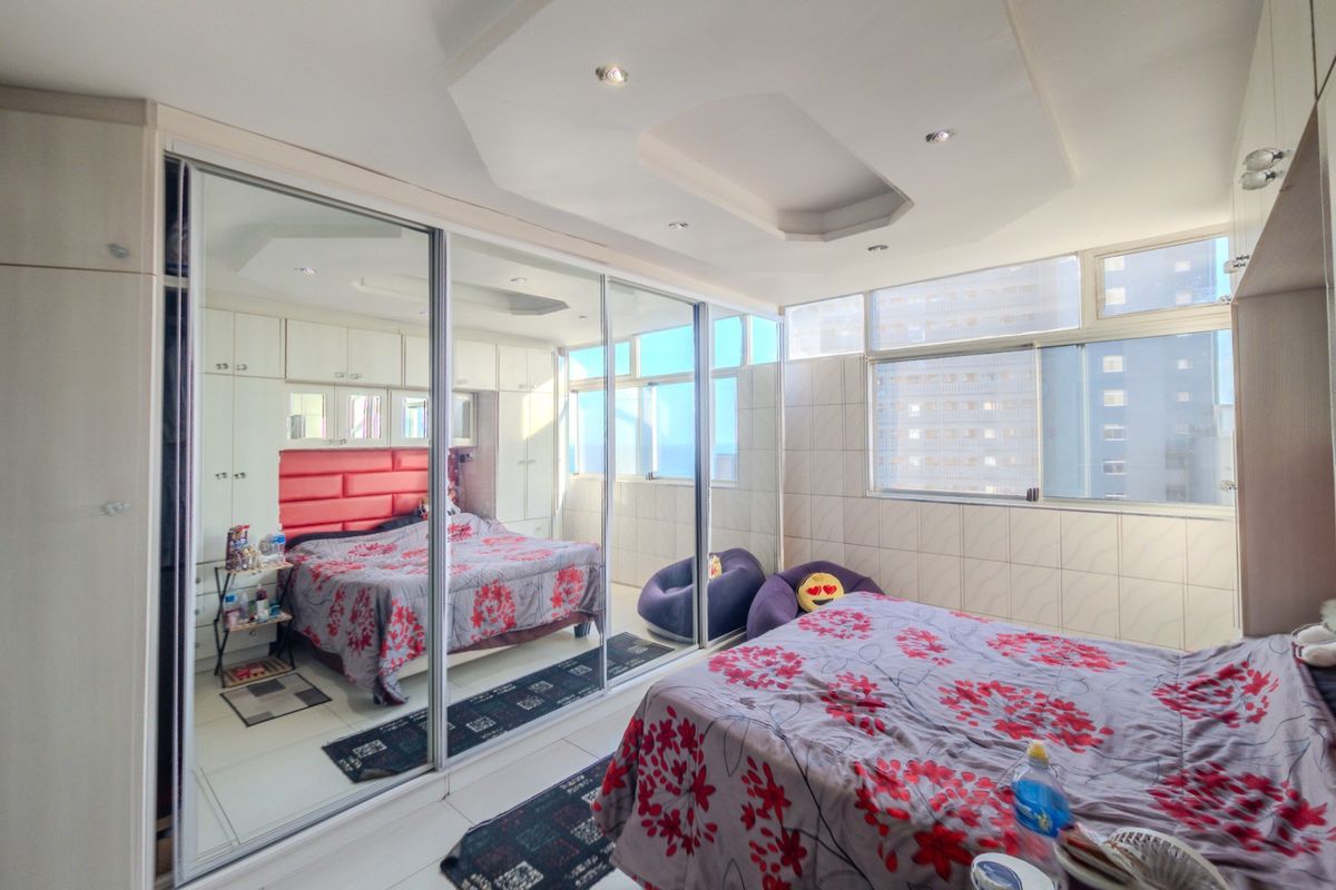A bedroom featuring extensive mirrored sliding wardrobes, built-in cabinetry, tiled wall finishes, and large windows providing natural light.