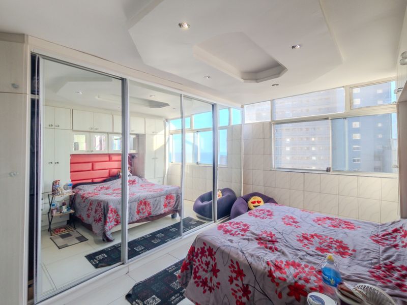 A bedroom featuring extensive mirrored sliding wardrobes, built-in cabinetry, tiled wall finishes, and large windows providing natural light.