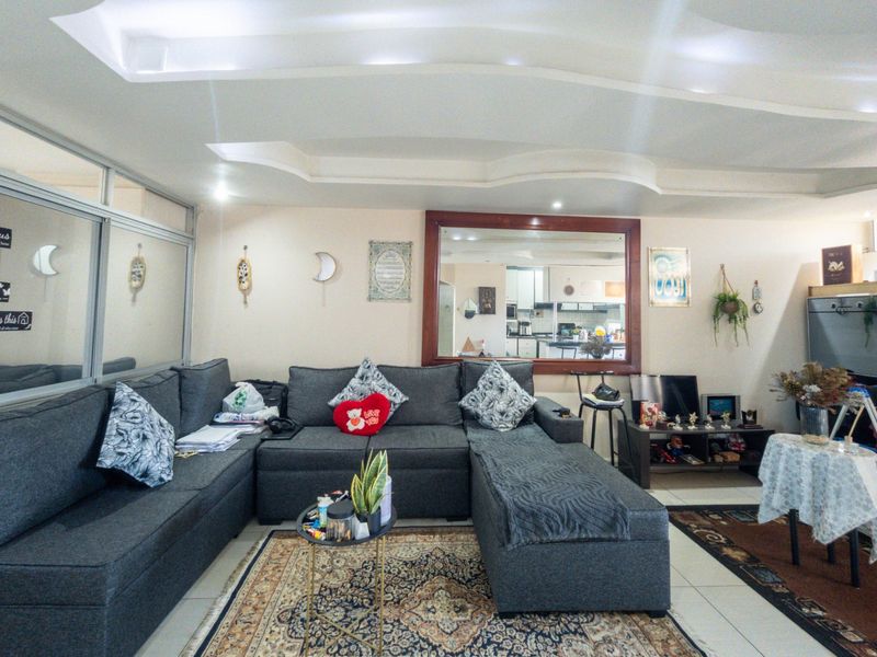 Open plan living area featuring tiled flooring, a decorative recessed ceiling, and an interior window looking through to the kitchen space.