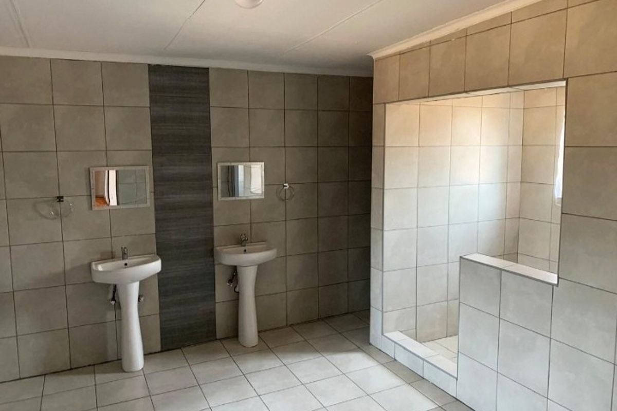 Spacious bathroom featuring dual pedestal wash basins and a large walk-in shower with neutral floor-to-ceiling tiling.