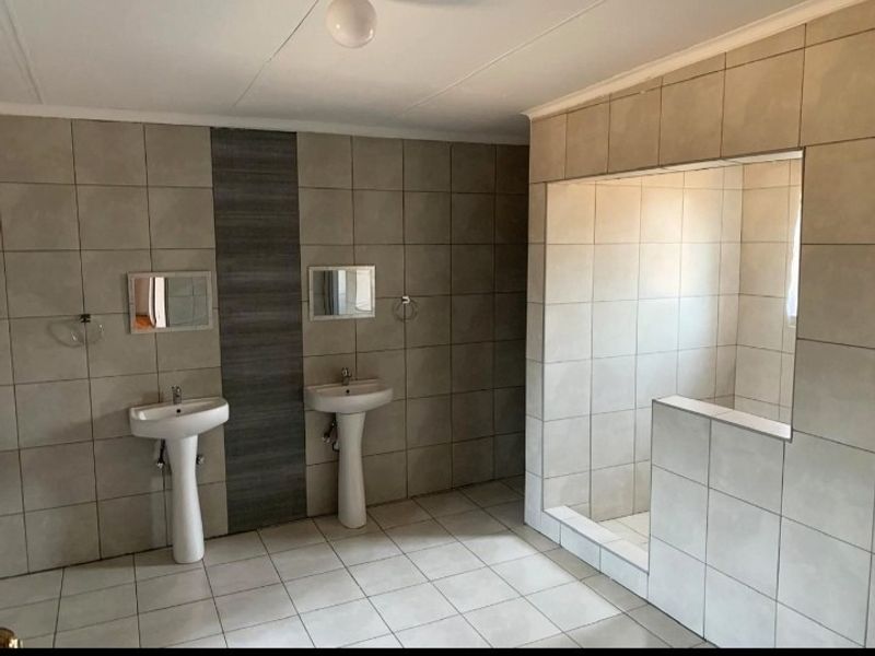 Spacious bathroom featuring dual pedestal wash basins and a large walk-in shower with neutral floor-to-ceiling tiling.