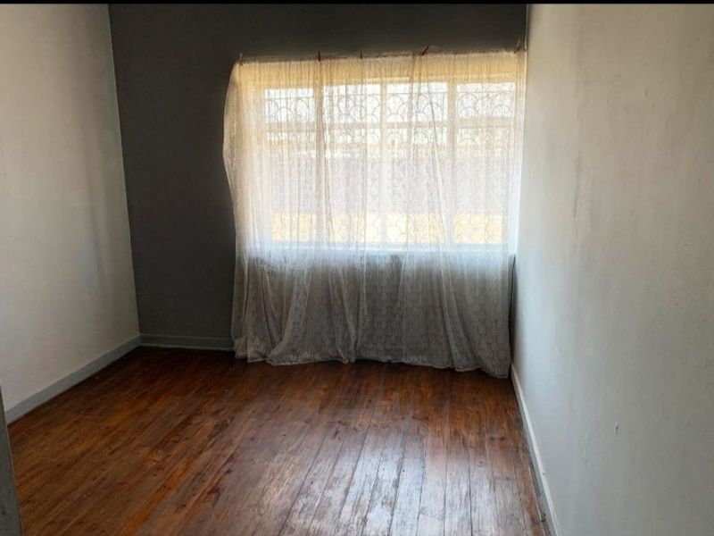 An empty bedroom featuring original wooden flooring and a window fitted with security bars, offering a blank canvas for renovation.