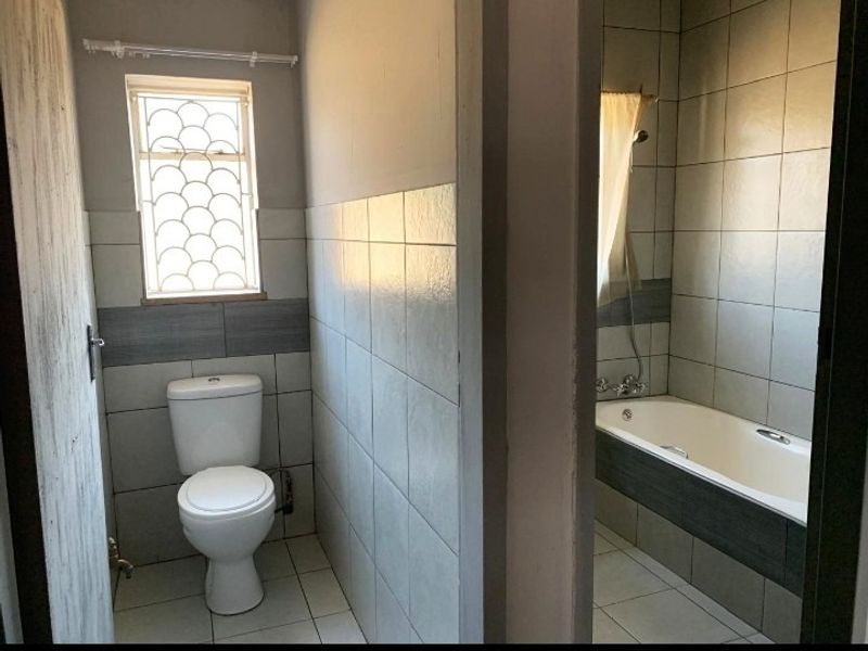A functional bathroom featuring a standard toilet and a bathtub with shower mixer, finished with neutral wall and floor tiling.