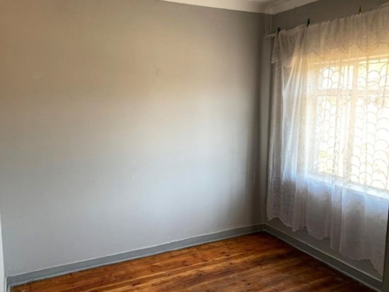 A vacant bedroom featuring original hardwood flooring, neutral wall paint, and a window fitted with security bars.