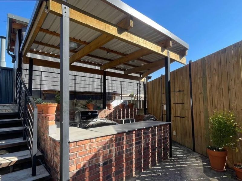 Outdoor entertainment area featuring a covered patio with a built-in brick barbecue, timber pergola, and staircase access.