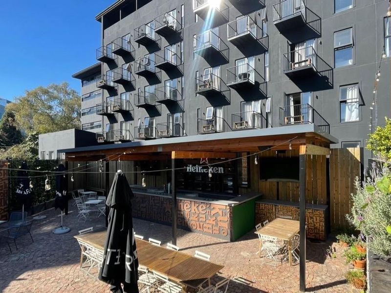 Outdoor entertainment area featuring a covered bar and paved courtyard, situated at the base of a multi-story apartment building with private balconies.
