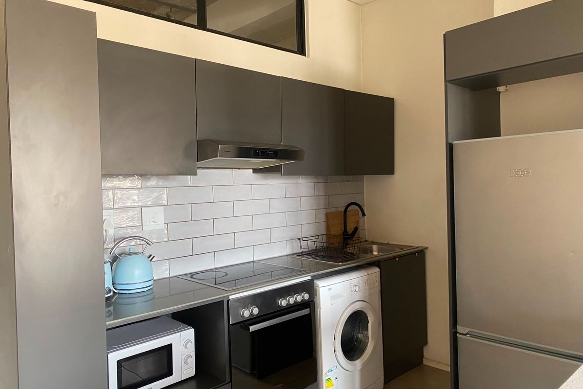 Modern kitchen featuring grey cabinetry, subway tile backsplash, integrated electric hob, oven, extractor fan, and a stainless steel sink with a black mixer tap.