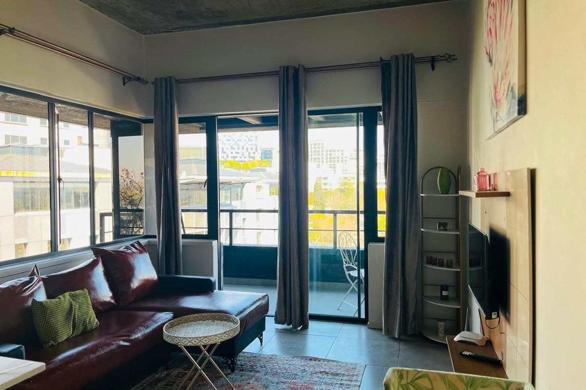 A bright living room featuring an exposed concrete ceiling, large windows, and sliding glass doors leading to a private balcony.