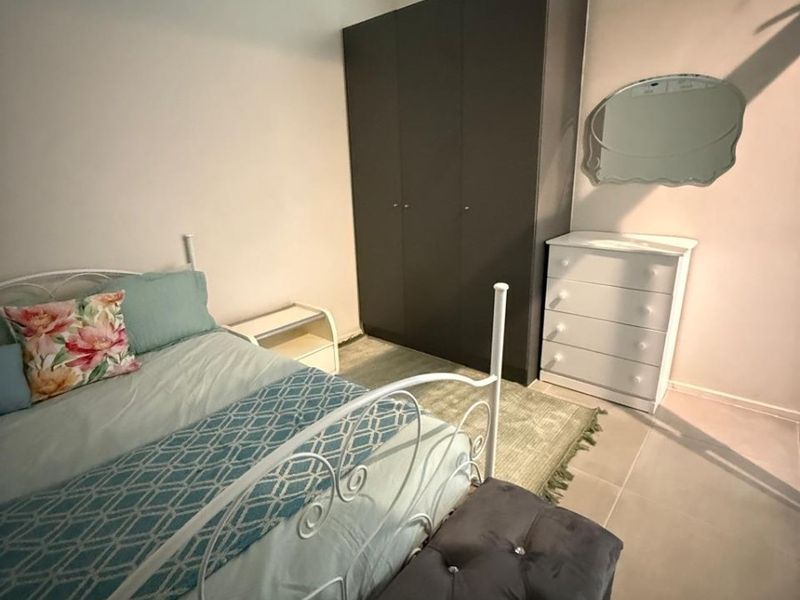 A bedroom featuring a built-in wardrobe, tiled flooring, and a high-level clerestory window providing natural light.