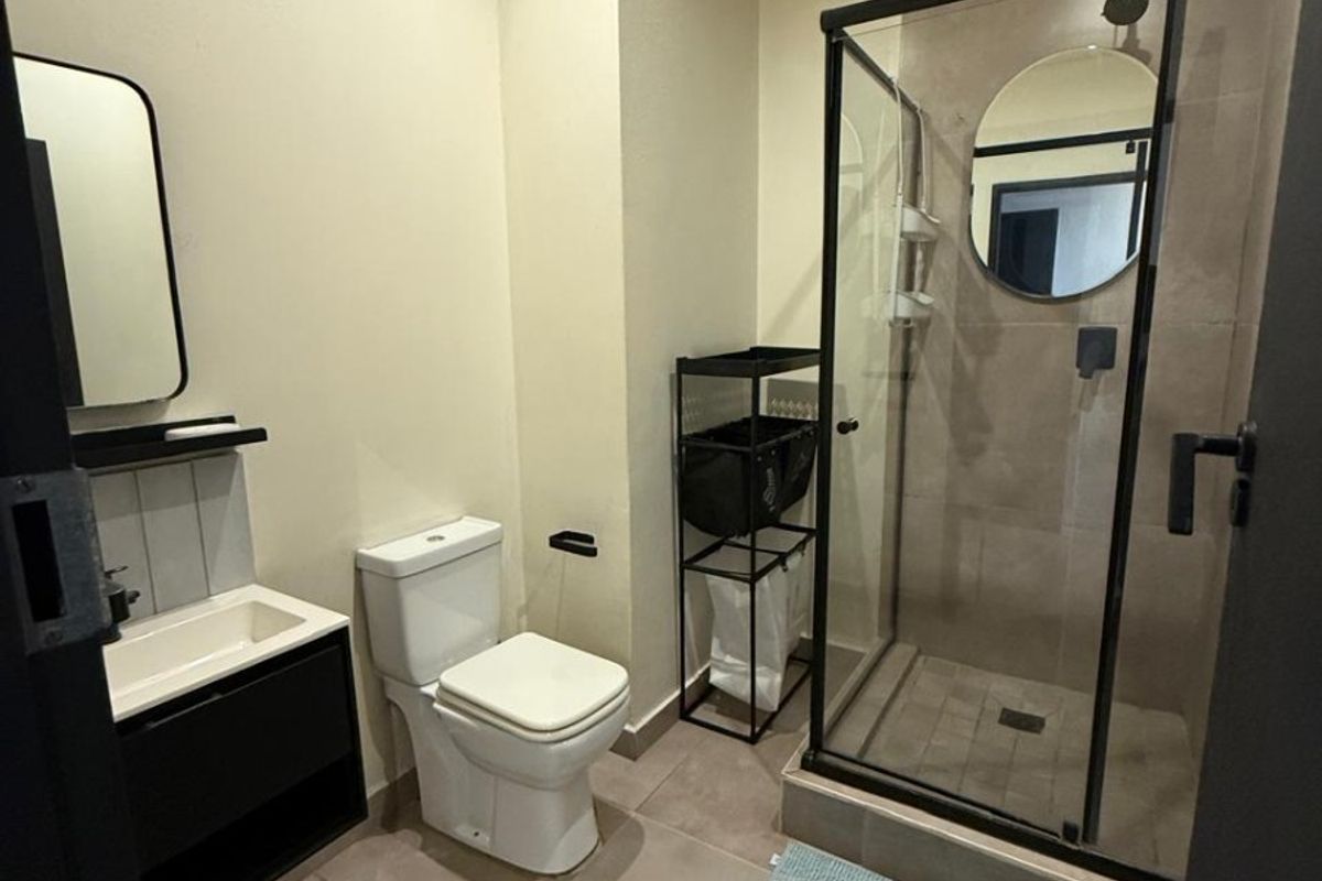 Modern bathroom featuring a walk-in shower with a glass enclosure, a sleek vanity cabinet with a basin, and a toilet, finished with neutral floor tiles.