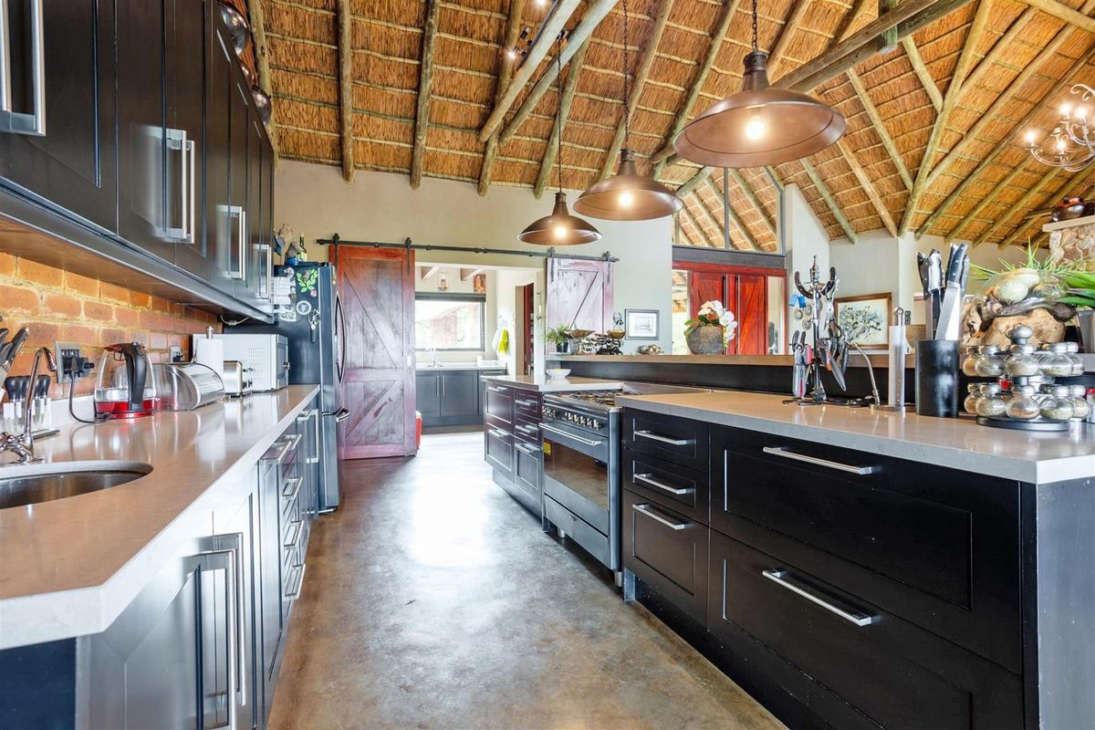 Spacious kitchen featuring a high exposed thatch ceiling, polished concrete floors, dark cabinetry, stone countertops, and a gas range cooker.