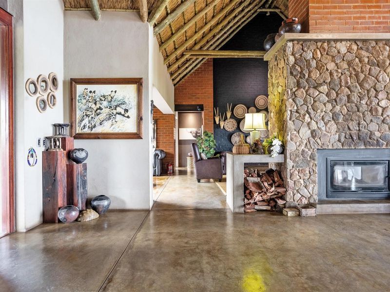 Spacious living area featuring a prominent stone fireplace, polished concrete floors, and an impressive exposed thatch roof with rustic brick accents.