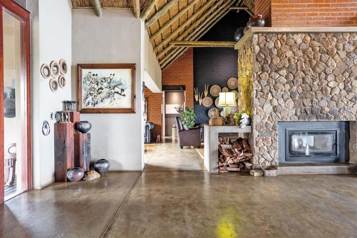 Spacious living area featuring a prominent stone fireplace, polished concrete floors, and an impressive exposed thatch roof with rustic brick accents.