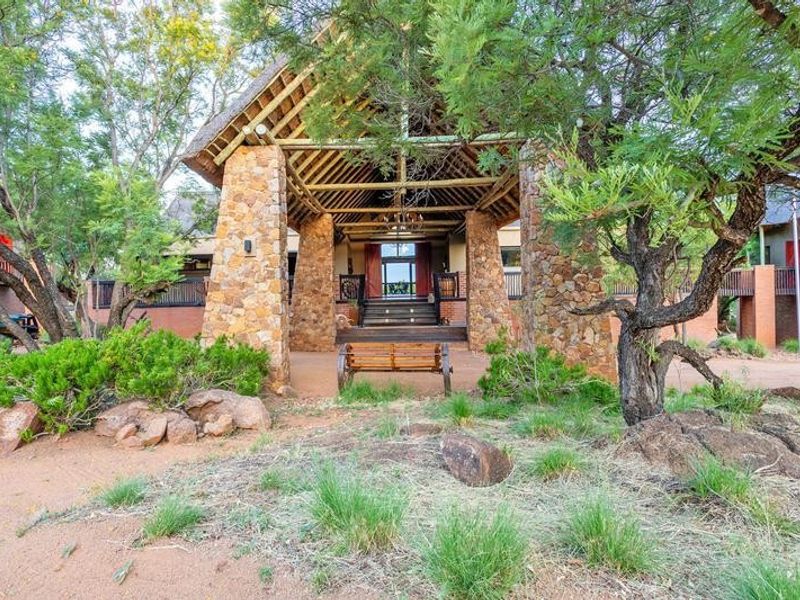A striking front entrance featuring prominent stone pillars, a high thatched roof with exposed timber trusses, and a raised deck leading to the main door.
