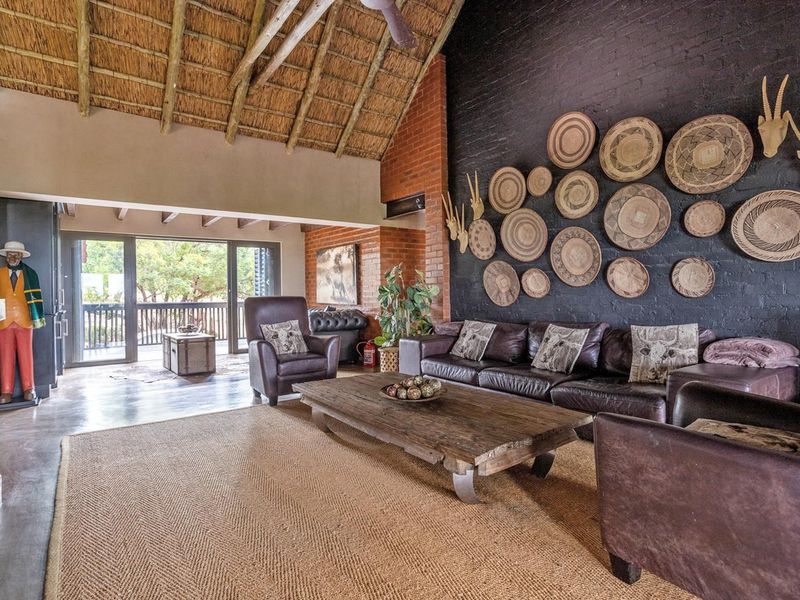 Spacious living room featuring a high exposed thatch ceiling, striking black brick feature wall, fireplace, and large sliding doors opening to an outdoor area.