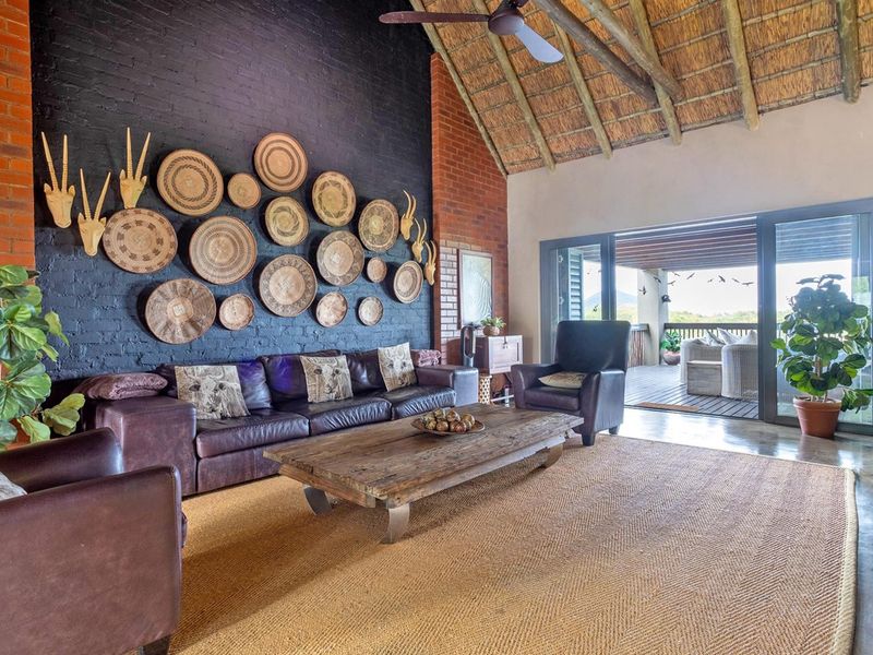 Spacious living room featuring a high thatched ceiling, exposed brick walls, polished concrete flooring, and large sliding doors opening to an outdoor patio.