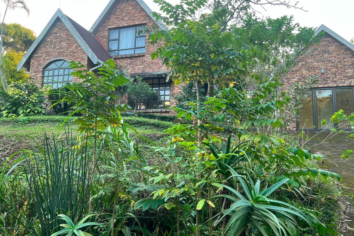A view of the rear face brick facade of the house, featuring a pitched roof design and established garden surroundings.