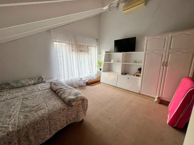 Spacious bedroom featuring a vaulted ceiling, built-in wardrobe, integrated shelving, and a wall-mounted air conditioning unit.