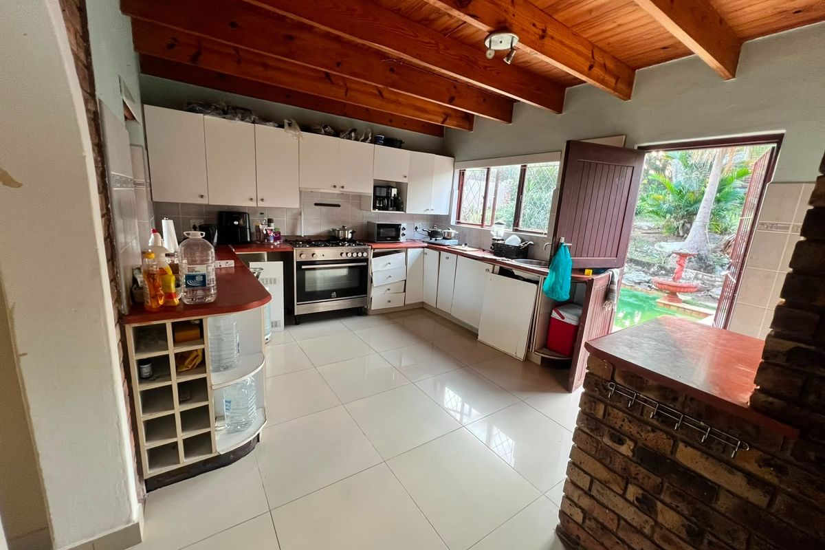 Kitchen featuring exposed timber beam ceilings, tiled flooring, built-in cabinetry, and a brick breakfast bar with direct access to the outdoor pool area.