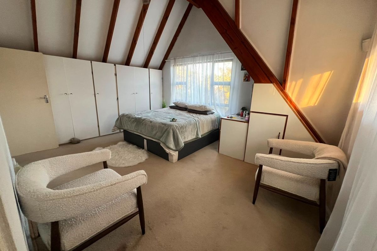 Spacious attic-style bedroom featuring exposed timber rafters, extensive built-in cupboard storage, and large windows allowing for natural light.