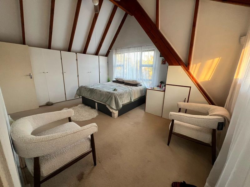 Spacious attic-style bedroom featuring exposed timber rafters, extensive built-in cupboard storage, and large windows allowing for natural light.