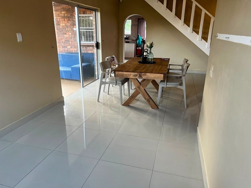 Open plan living and dining area featuring polished porcelain floor tiles, a staircase, and direct access to an outdoor patio through sliding glass doors.