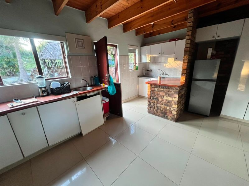 A functional kitchen featuring exposed timber ceiling beams, a rustic brick breakfast bar, tiled flooring, and ample built-in cabinetry with a tiled splashback.