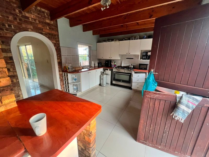 Kitchen featuring exposed timber ceiling beams, a brick feature wall, tiled flooring, and built-in cabinetry with a gas stove and tiled backsplash.