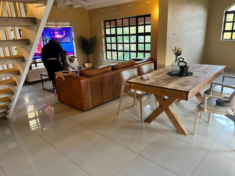 Open-plan living and dining area featuring large grid-pattern windows, polished floor tiles, and an internal staircase.