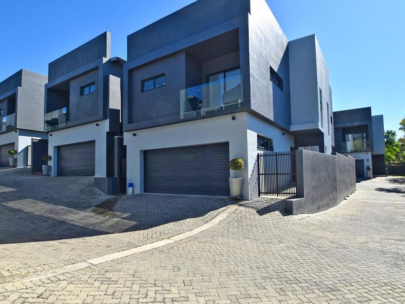 Modern double-storey townhouse exterior featuring a paved driveway, automated garage, and contemporary architectural design with glass balcony balustrades.