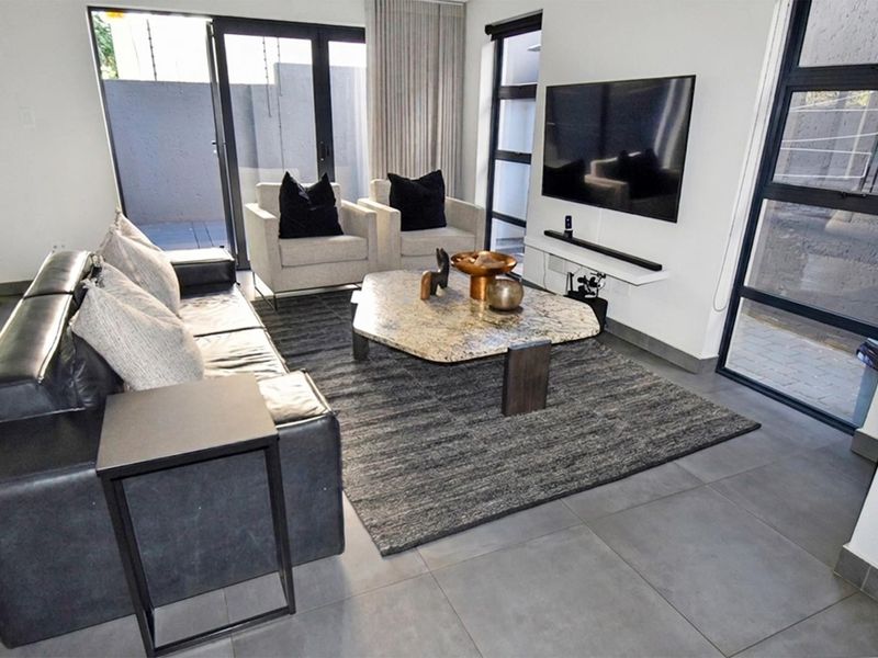 Modern living room featuring large format floor tiles, expansive aluminium framed sliding doors, and a wall-mounted television setup with a floating shelf.