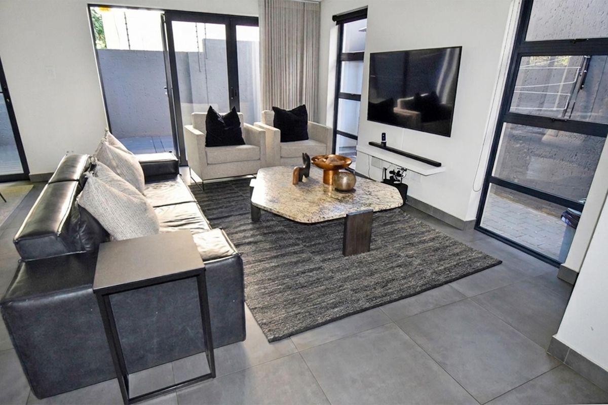 Modern living room featuring large format floor tiles, expansive aluminium framed sliding doors, and a wall-mounted television setup with a floating shelf.